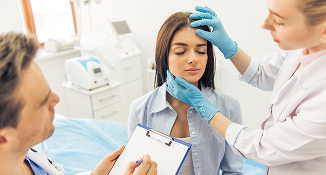 Mdico y enfermera revisando la cabeza y cuello de paciente.